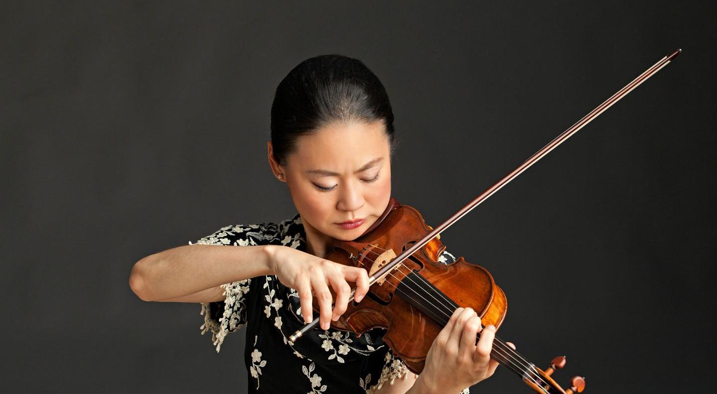 Violinist Midori plays her violin against a dark grey background