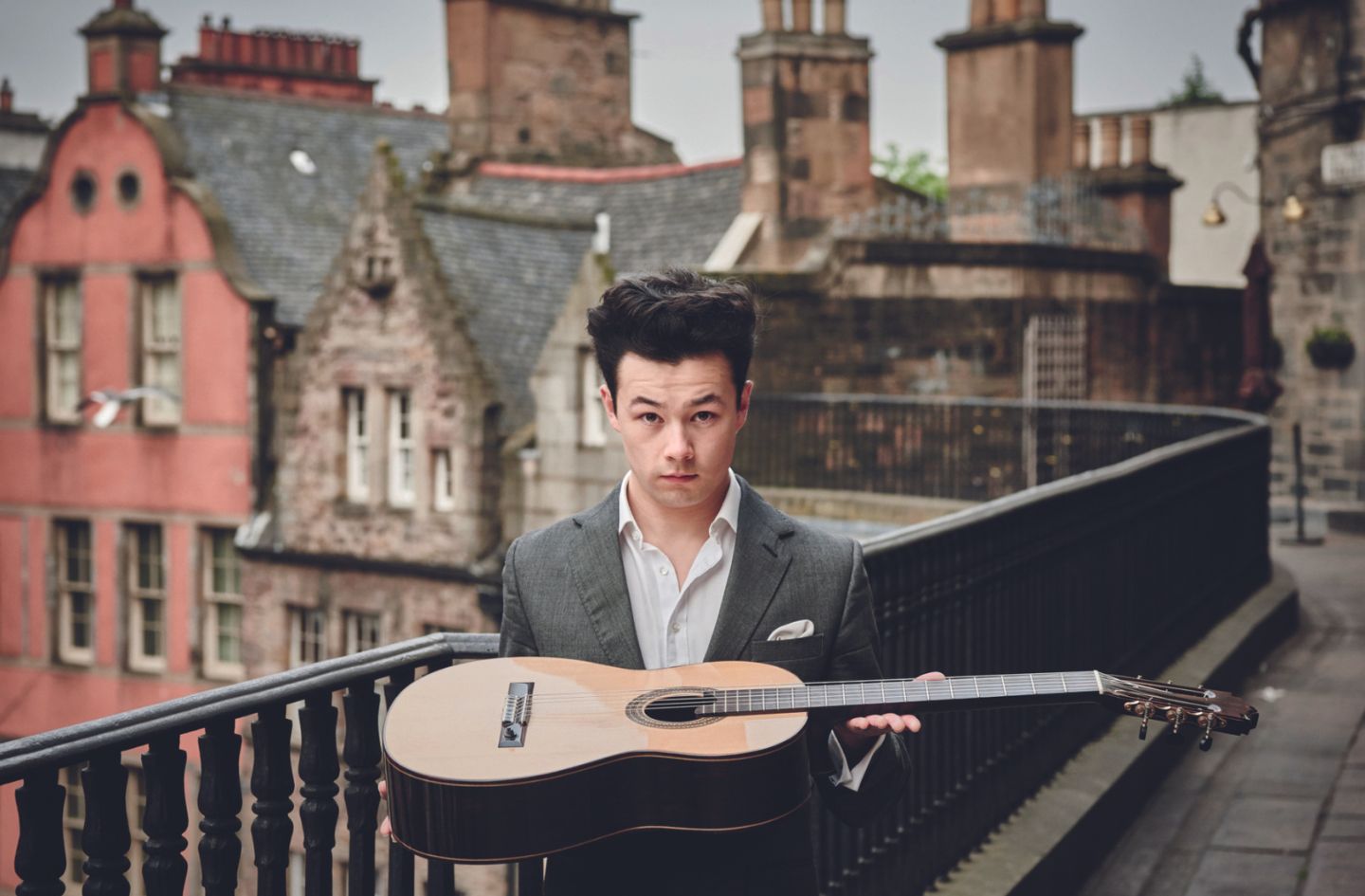 an image of Sean Shibe holding his acoustic guitar, standing on Edinburgh's Victoria Street