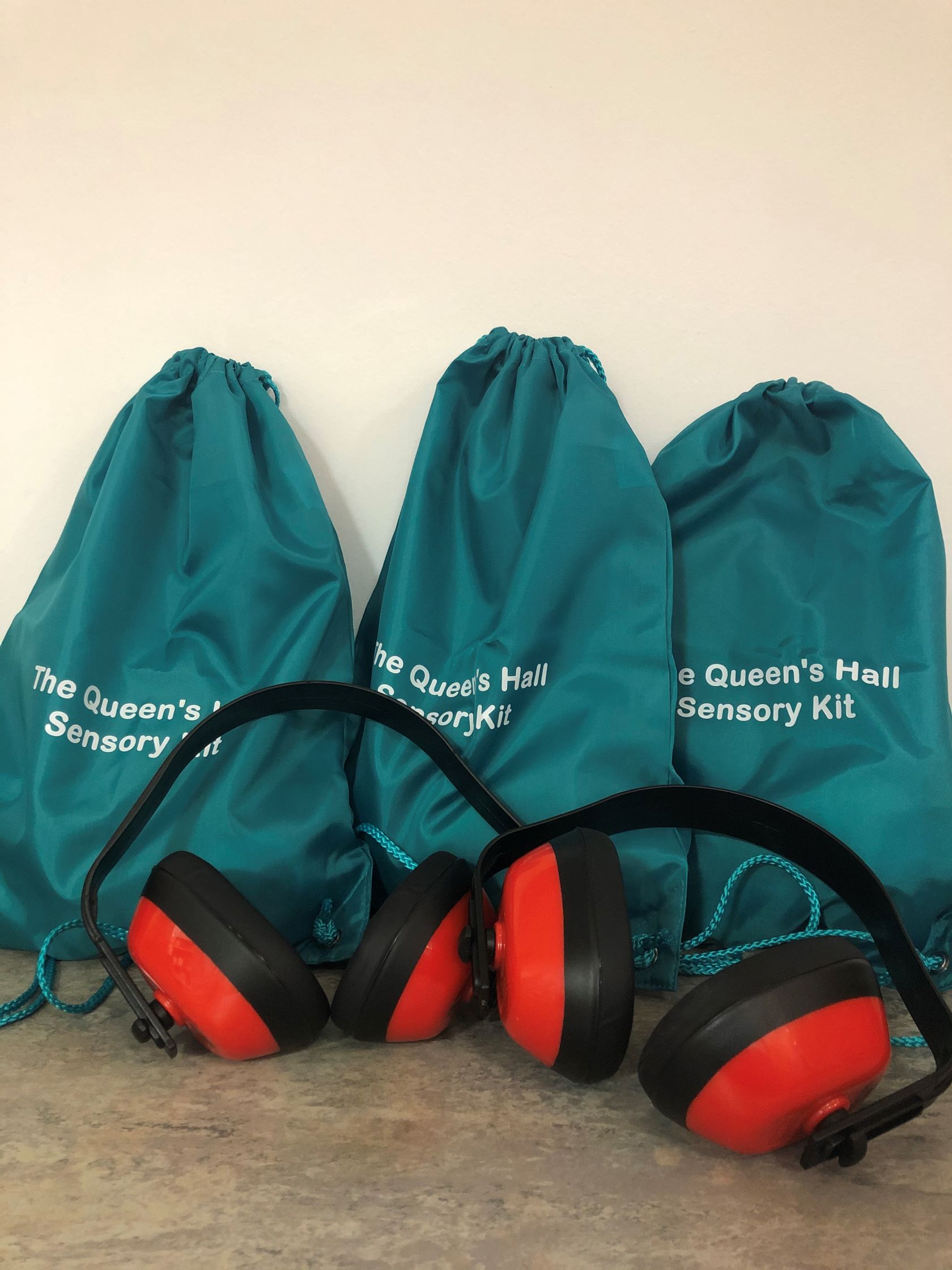 Three green bags with white writing saying The Queen's Hall Sensory Kit and three sets of ear denfenders