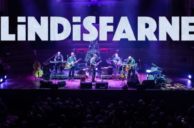 A view of a rock band on stage from a distance with the word Lindisfarne above their heads