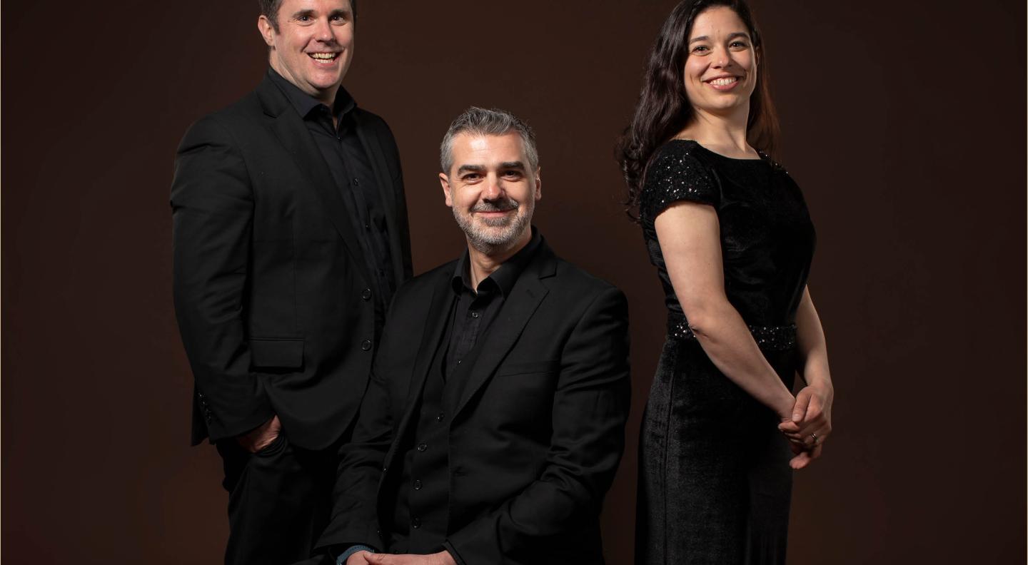 three members of the choir pose against a dark red background wearing black clothes