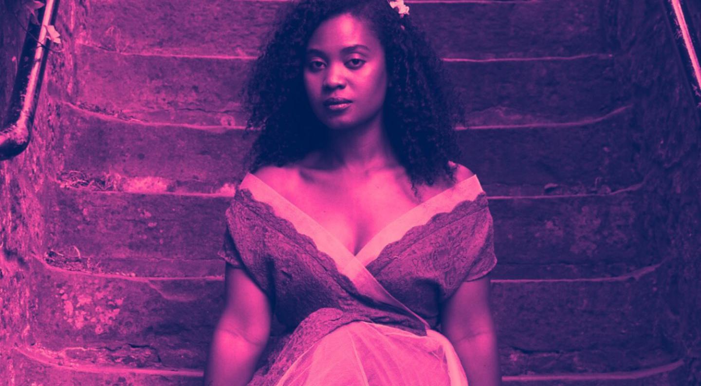 an image of Fifidiny in a white dress, tinted pink. She is sitting on stairs and has a flower crown on her hair.