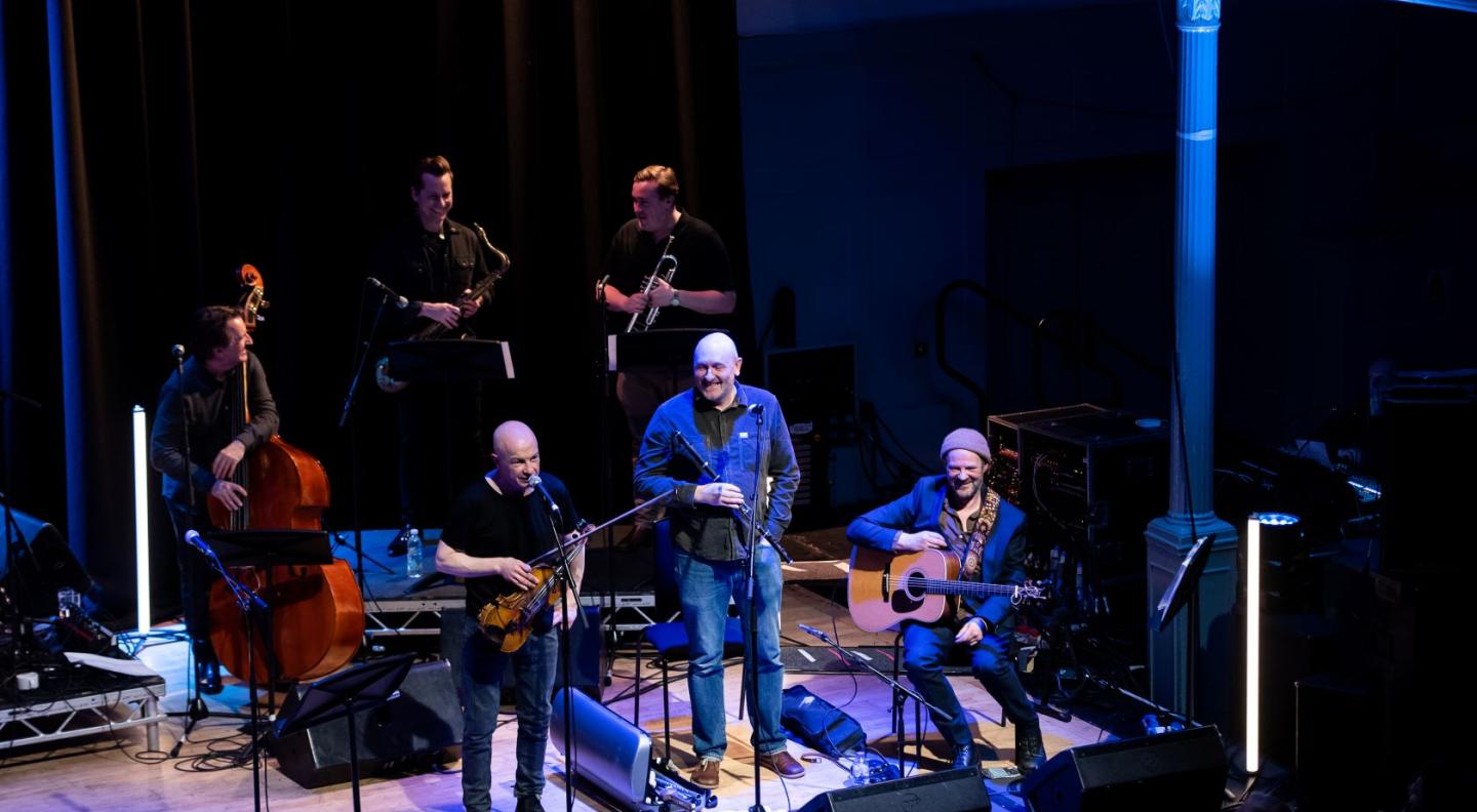 A view of The Queen's Hall stage from a distance with various artists playing traditional instruments