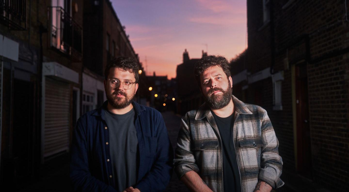 an image of the two members of the band standing side by side on a street at sunset