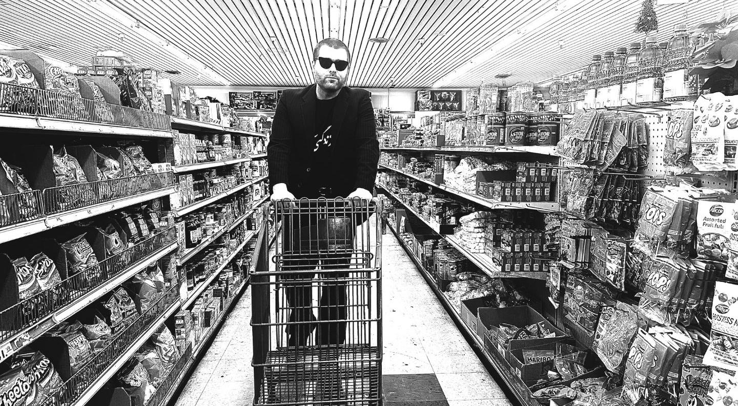 a black and white image of Callum in a supermarket, pushing a trolley