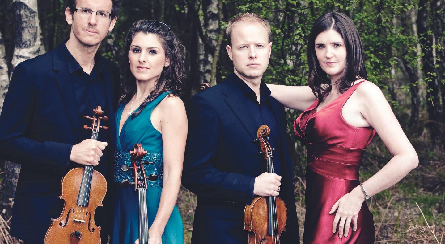 an image of the string quartet holding their instruments in front of a background of trees