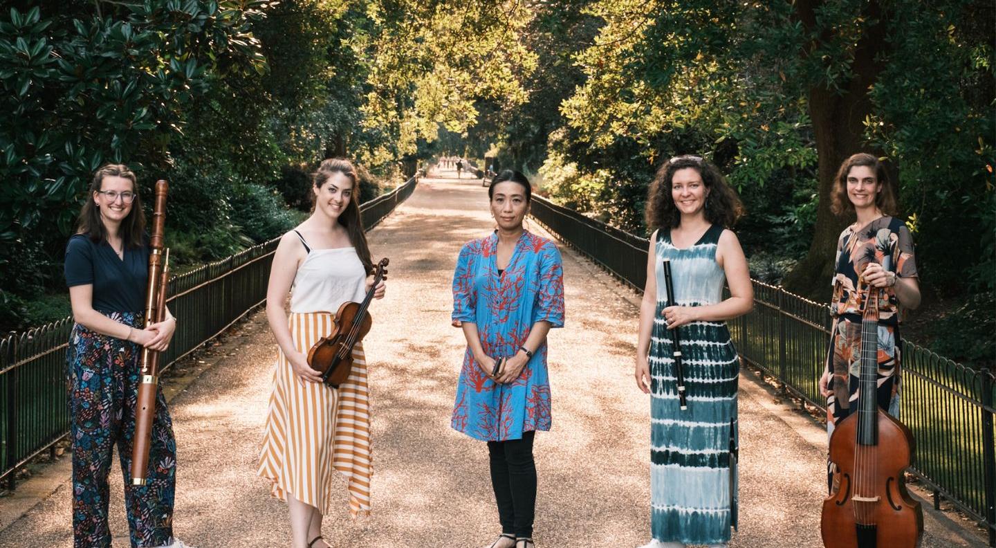 the ensemble standing in a park holding their instruments