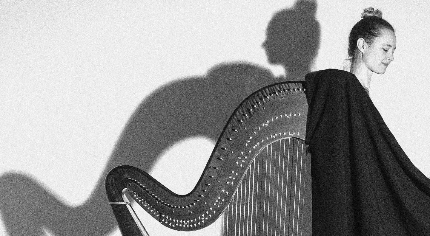 a black and white image of Esther Swift and her harp, casting a shadow on white wall