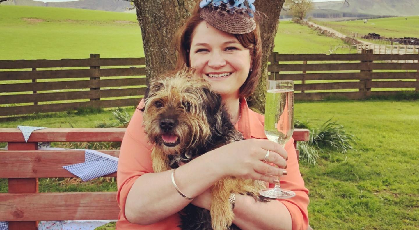 Gill Sims sits on a bench outdoors and holds her small terrier.