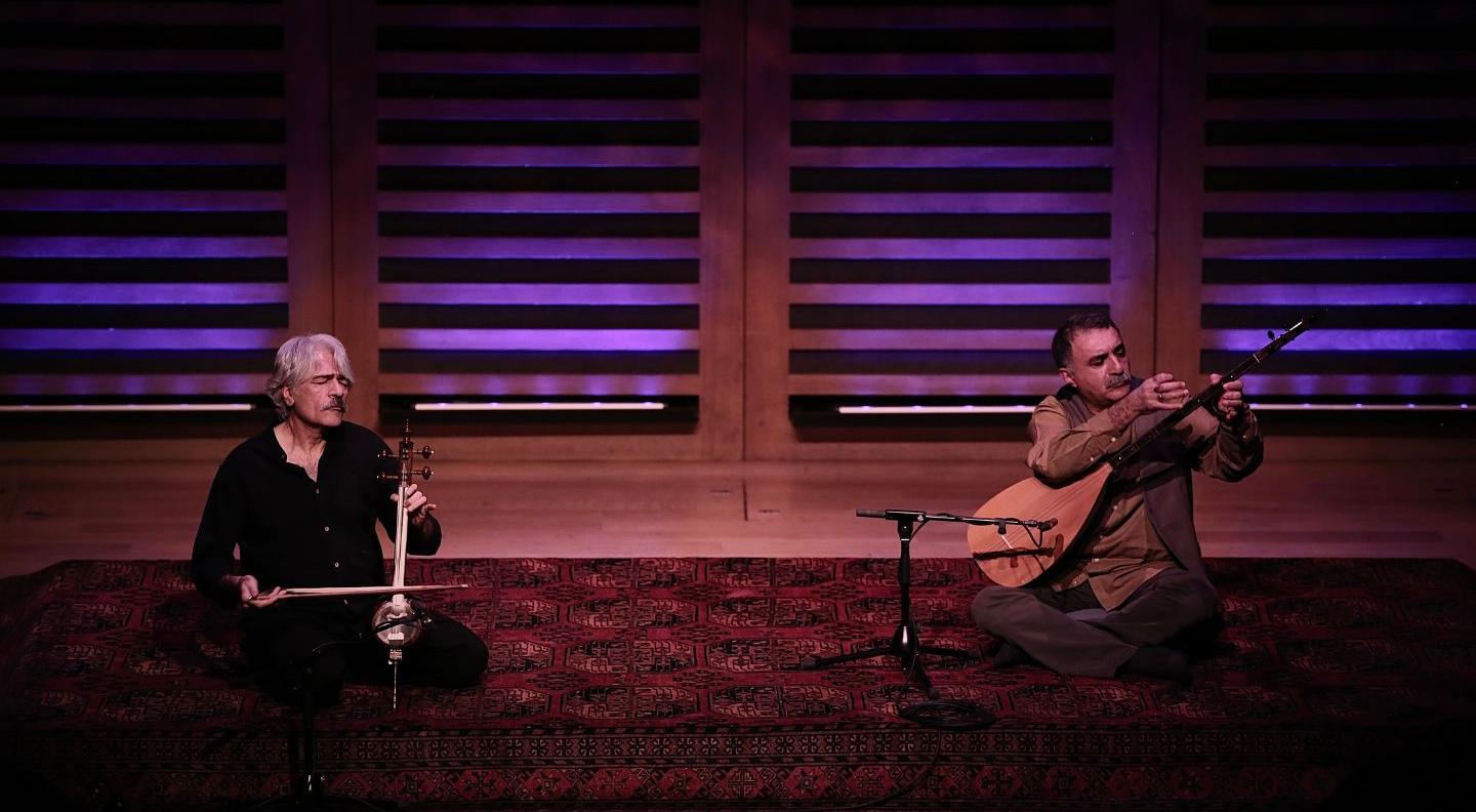 An image of Kayhan Kalhor & Erdal Erzincan on stage, sat down on a rug with their instruments