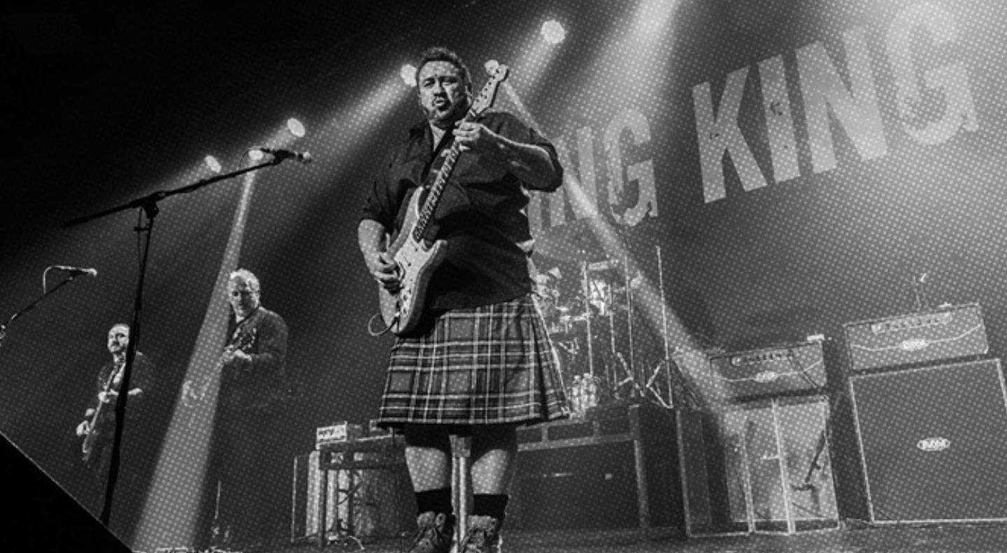 a black and white image of a guitarist wearing a kilt on stage