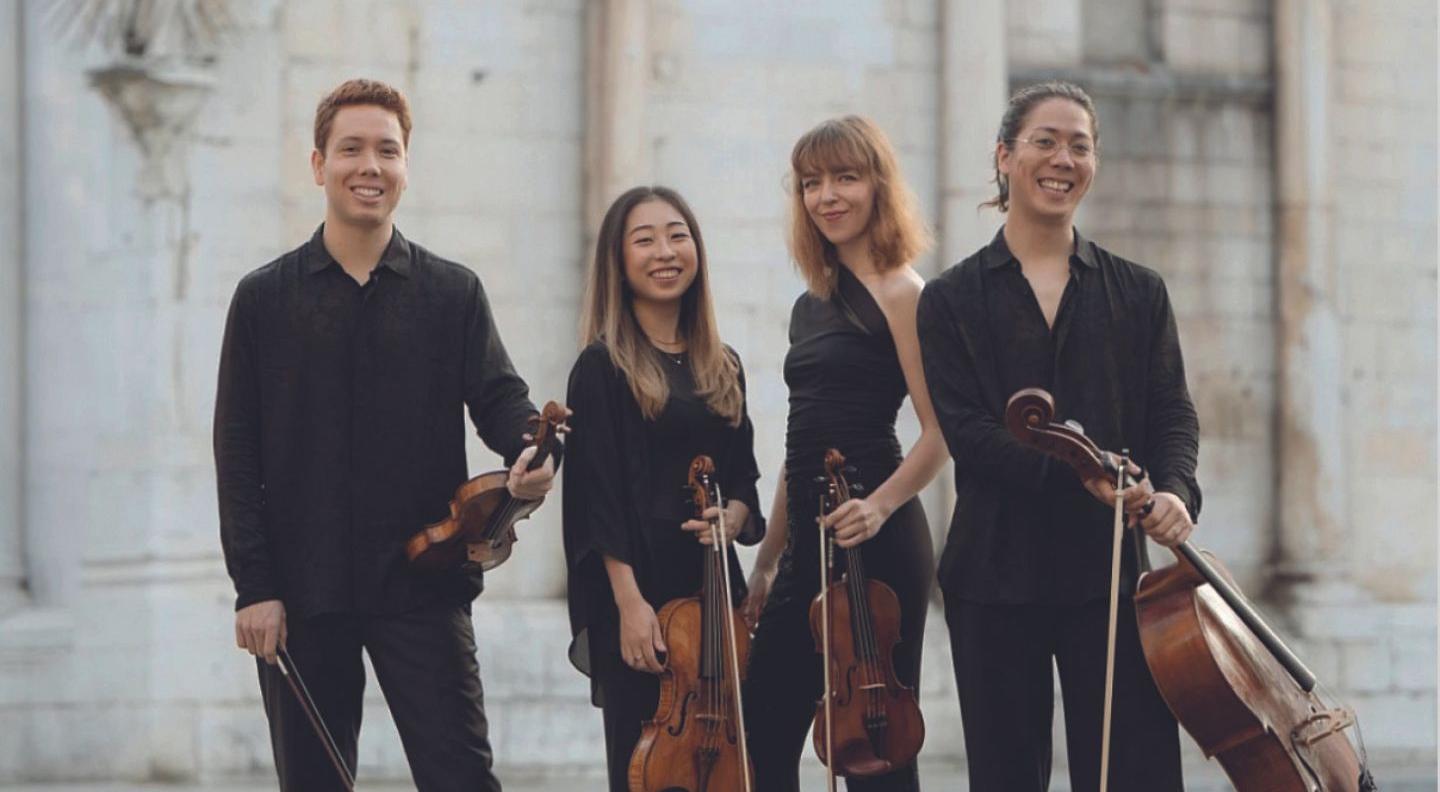 an image of the string quartet in front of a stone wall, holding their instruments