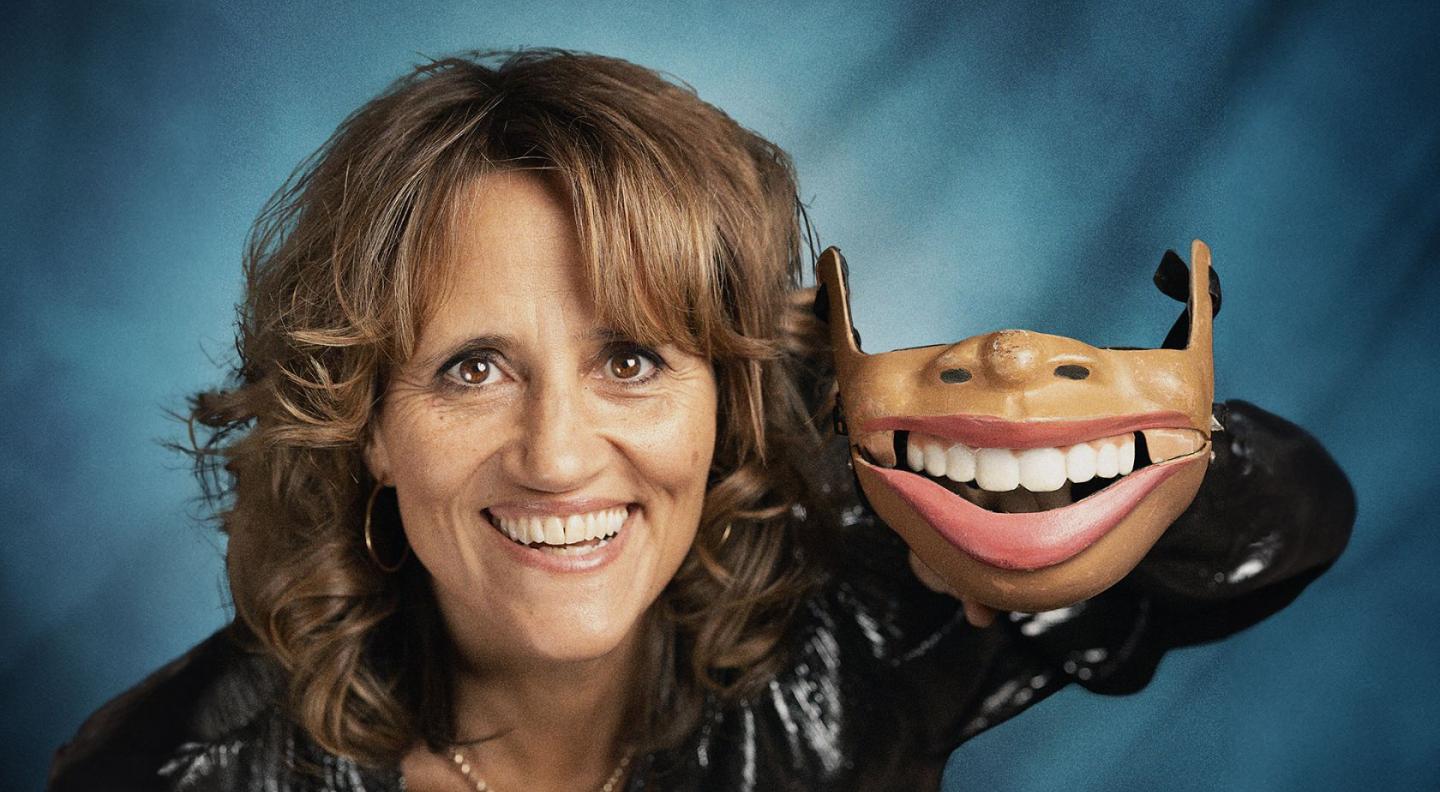 an image of Nina Conti, a woman with brown hair, holding a realistic-looking jaw mask