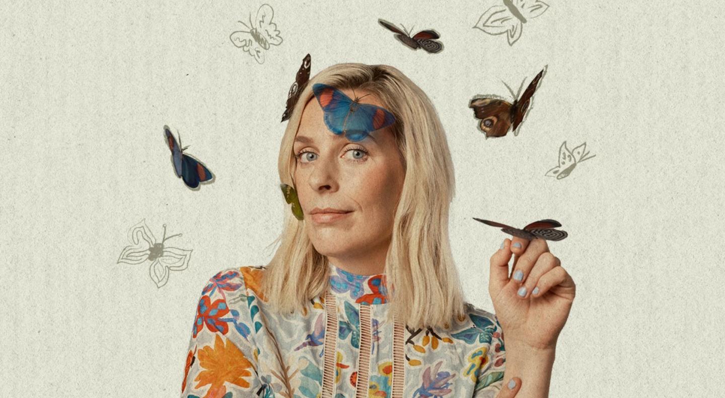 Comedian Sara Pascoe, a white female with shoulder length blonde hair, standing in front of a white background, with several different coloured butterflies around her.