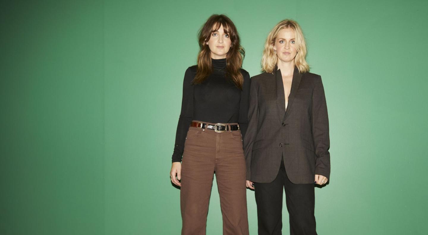 The two members of Ward Thomas, Catherine and Lizzy, standing in front of a green background